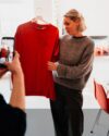 Eibe Obermeyer präsentiert ein rotes T-Shirt auf einem Kleiderbügel, während eine andere Person das Kleidungsstück mit dem Smartphone fotografiert.